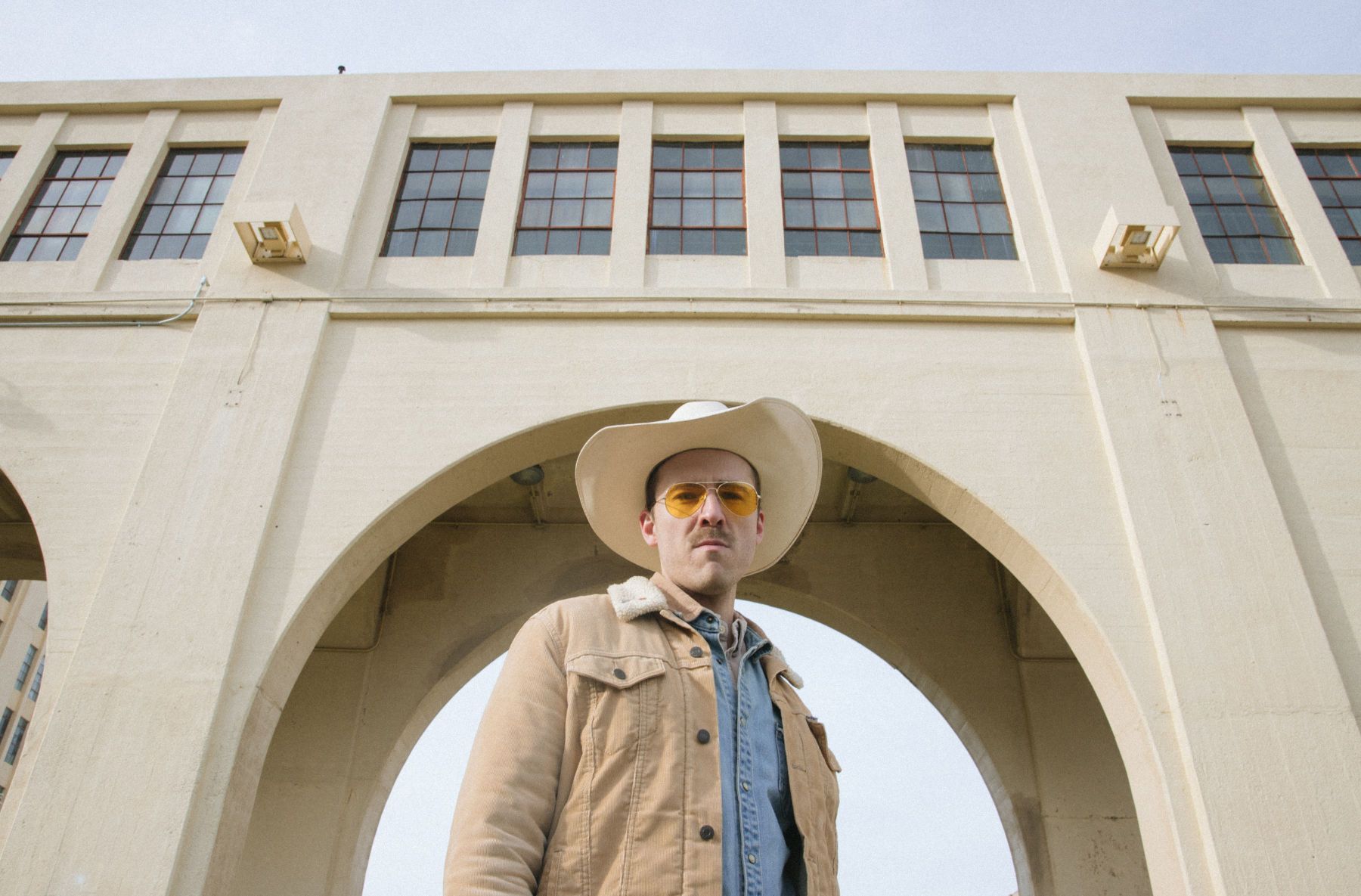 Dale Hollow is standing in his signature cowboy hat in front of an arch, looking down at the camera.