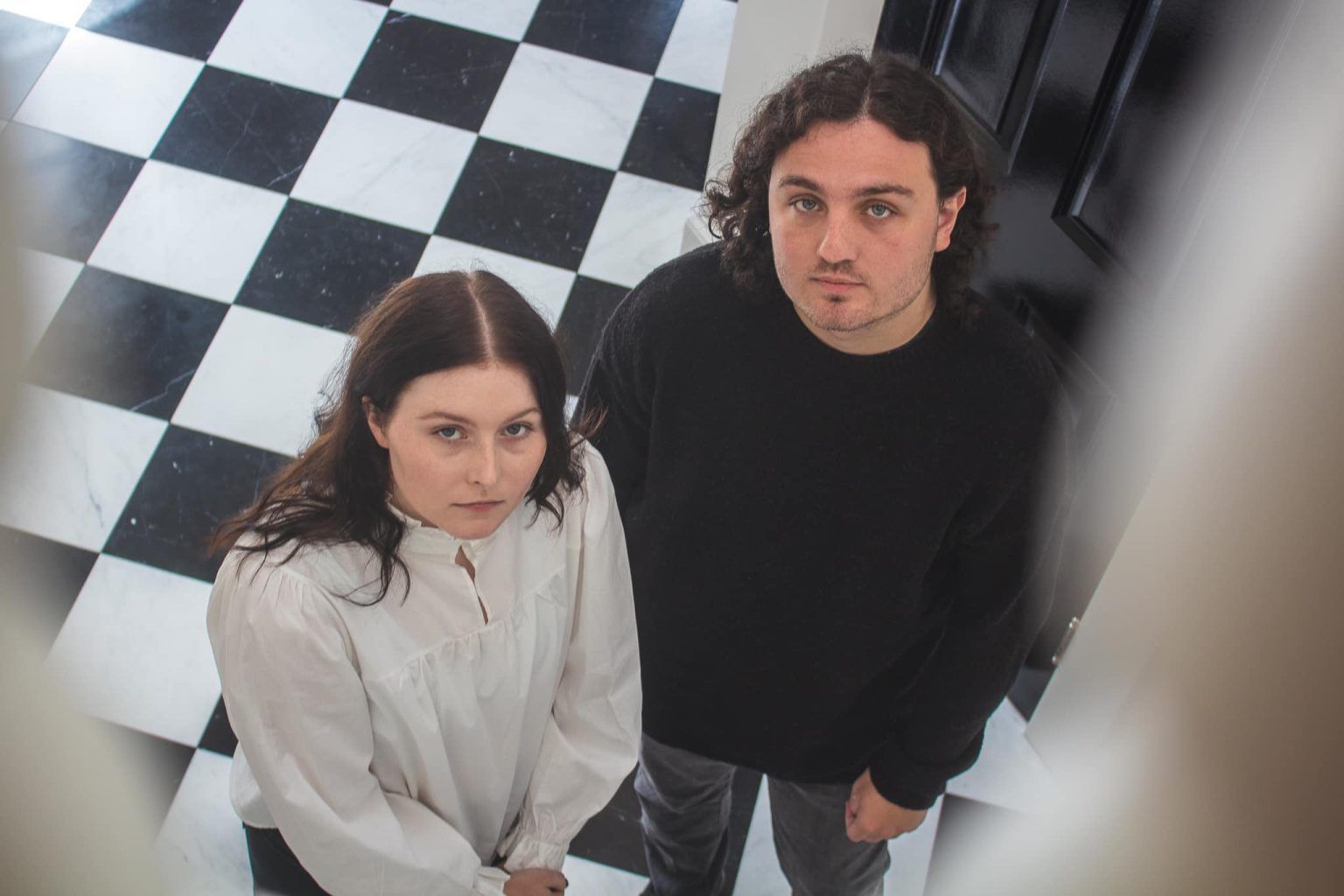 GLOSSER standing on a checkered floor looking up at the camera.