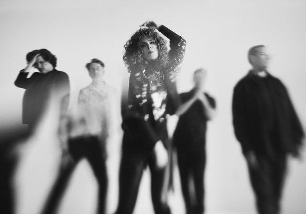 A black and white image of the band, standing behind a light flare.